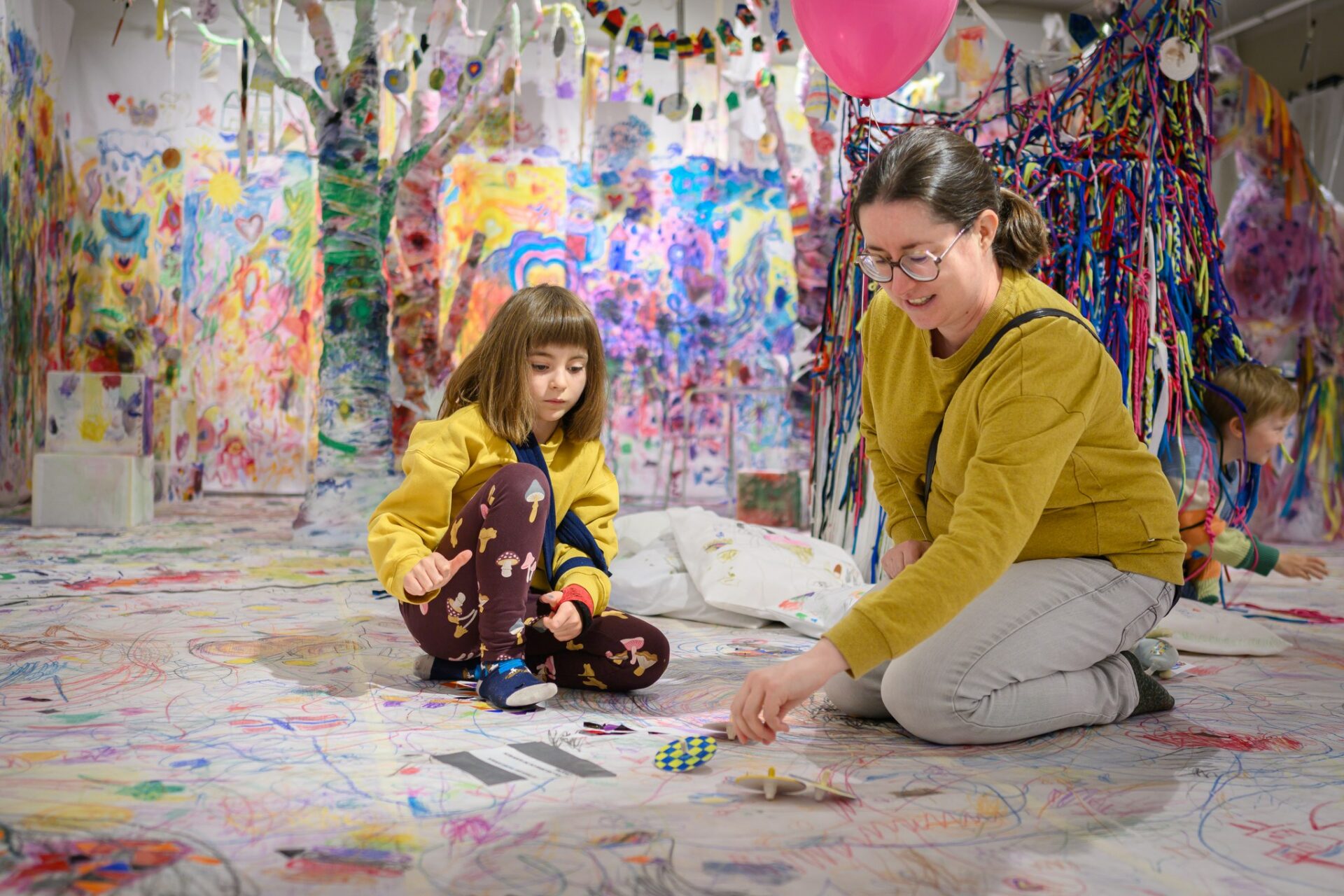 An adult and a child playing in a colorful room filled with art.